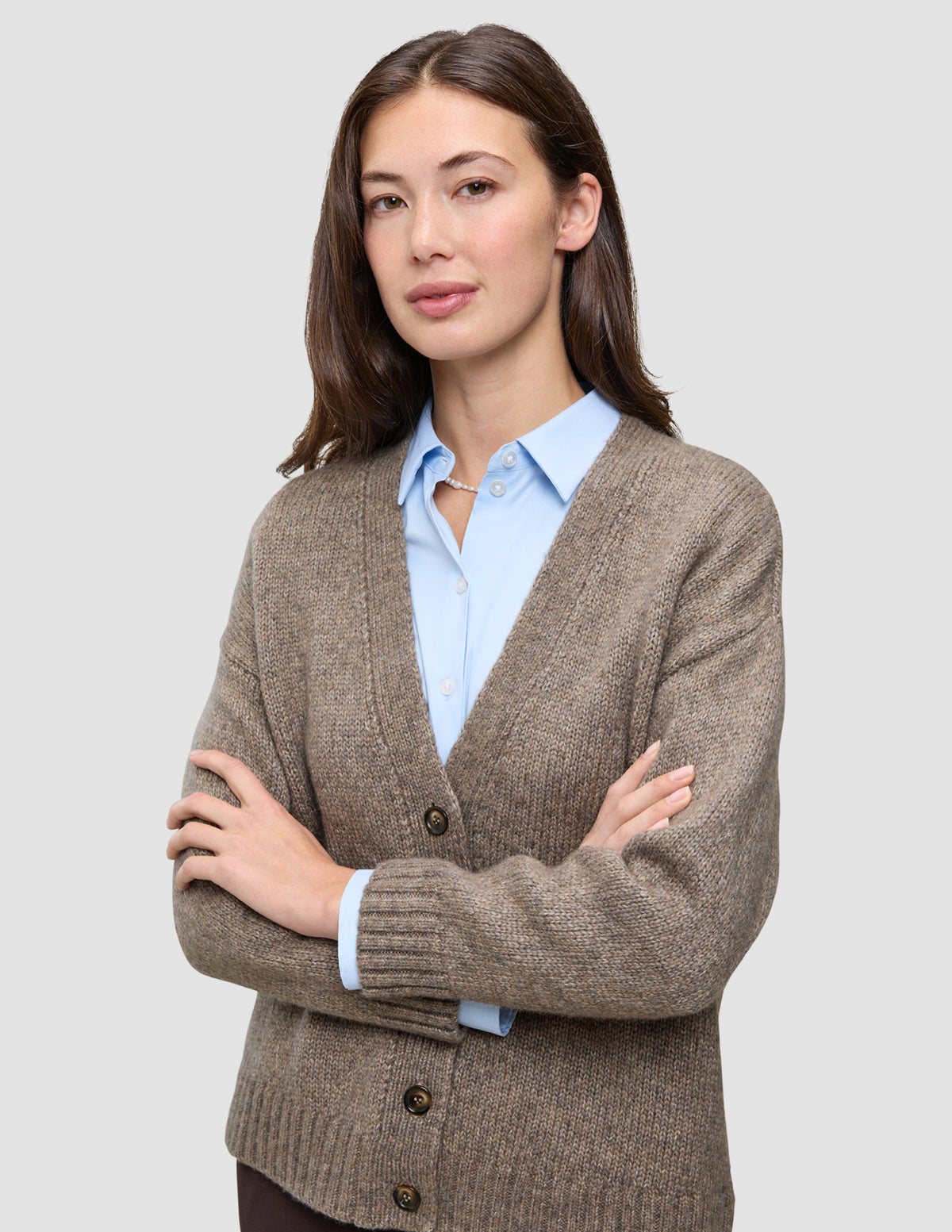 En kvinde iført en tyk, blød uldstrikket cardigan i farven taupe melange over en lyseblå skjorte med knapper.