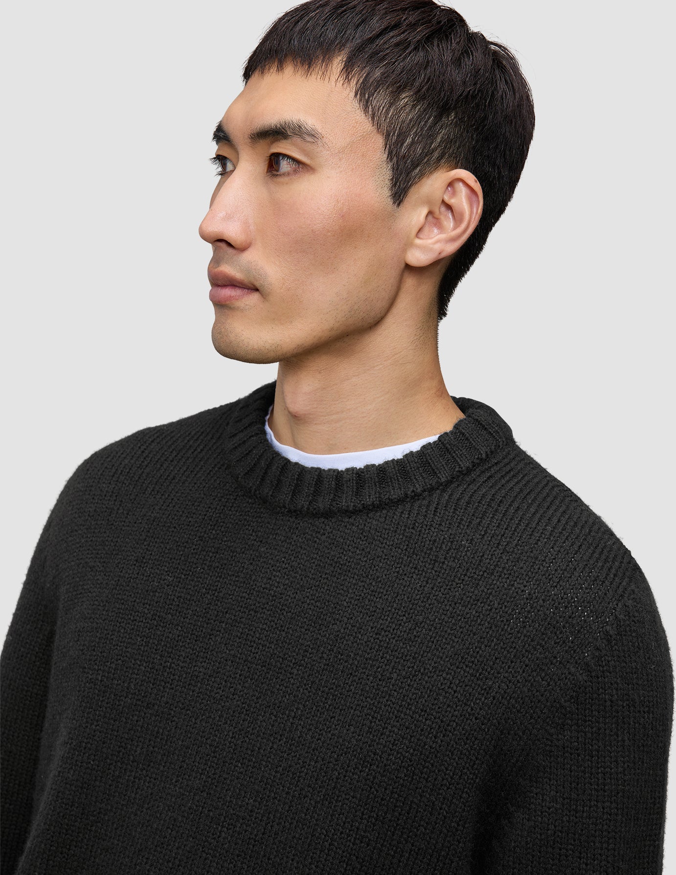 En mand iført en sort, tyk, blød uldtrøje med rund hals over en hvid skjorte, der fremhæver klassisk dansk design.