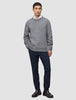 En mand iført en tyk, blød uldstrikket sweater med rund hals i farven Glacier Grey over en hvid skjorte med krave, marineblå bukser og loafers.