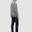Set fra siden: En person iført en grå, tyk, blød uldstrikket sweater med rund hals i farven Glacier Grey, mørke bukser og mørke loafers.