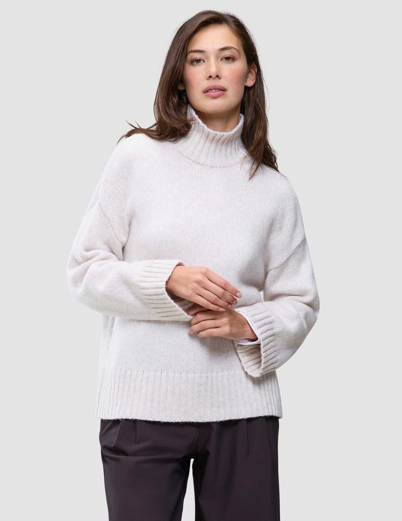 En kvinde har en Women’s Chunky Soft Wool Knit Turtleneck Sugar Melange på, en oversized, off-white trøje i grovstrikket design.