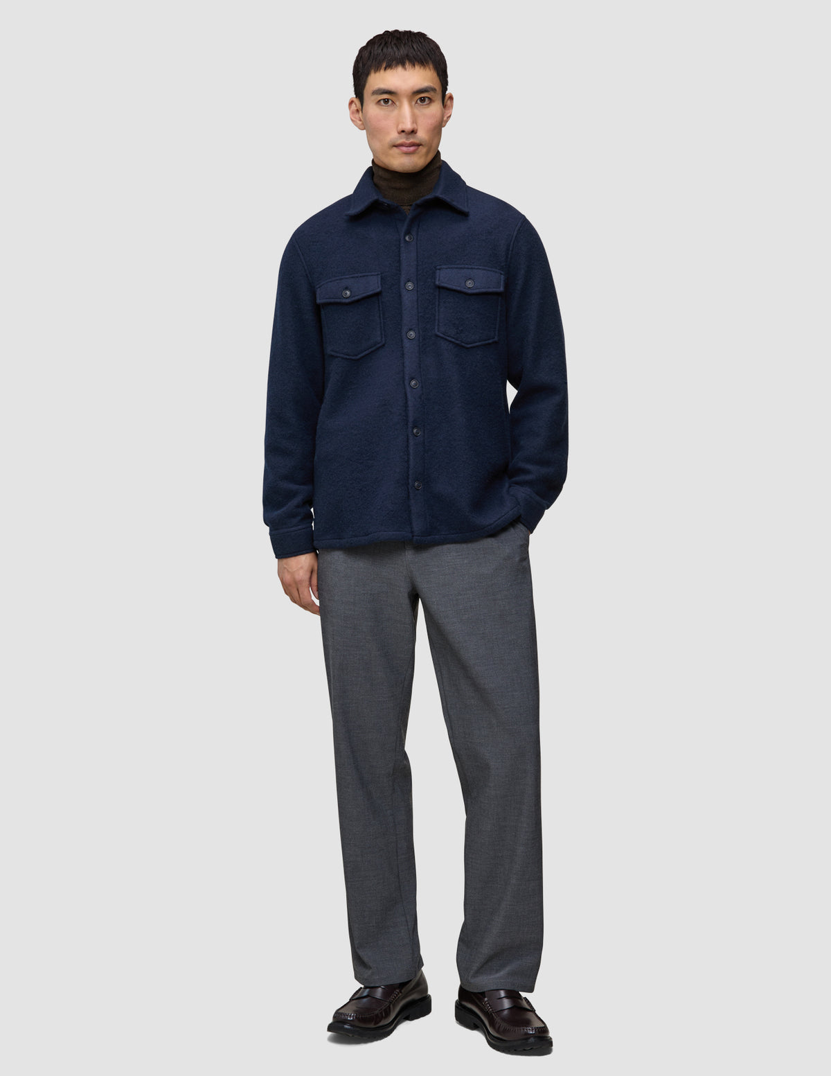 En person, der bærer en dobbeltlags uldskjorte i mørk marineblå i regular-pasform over en mørk sweater, grå bukser og mørke loafers.