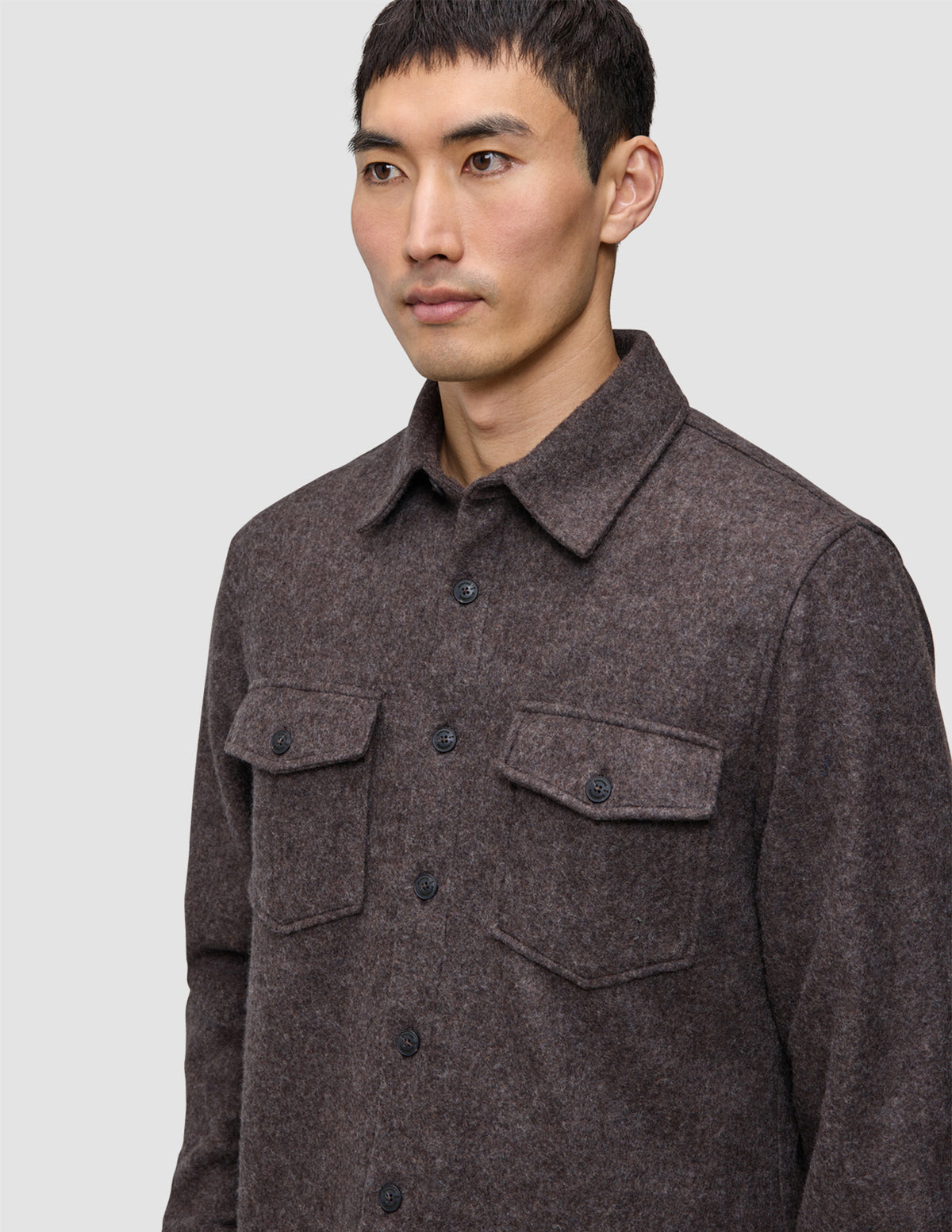 En person, der bærer en brun, langærmet Double Layer Wool Overshirt med knapper og to brystlommer.