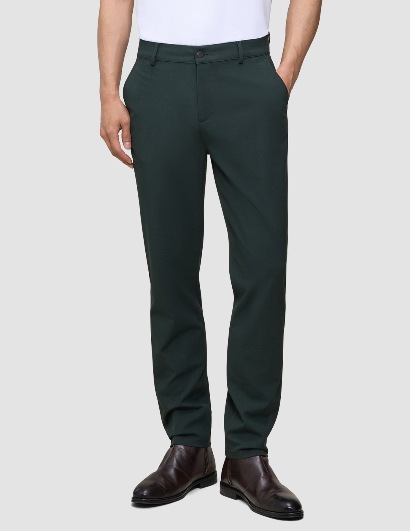 En person iført mørkegrønne Ease Pants Regular Northern Pine-bukser og mørke læderstøvler.