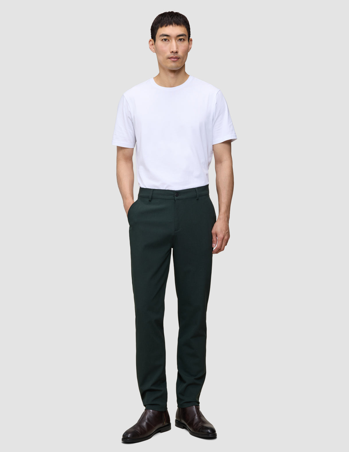 En mand iført en hvid T-shirt, Ease Pants Regular Northern Pine og brune læderstøvler.