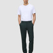 En mand iført en hvid T-shirt og mørkegrønne Ease Pants Regular Northern Pine med hænderne i lommerne.