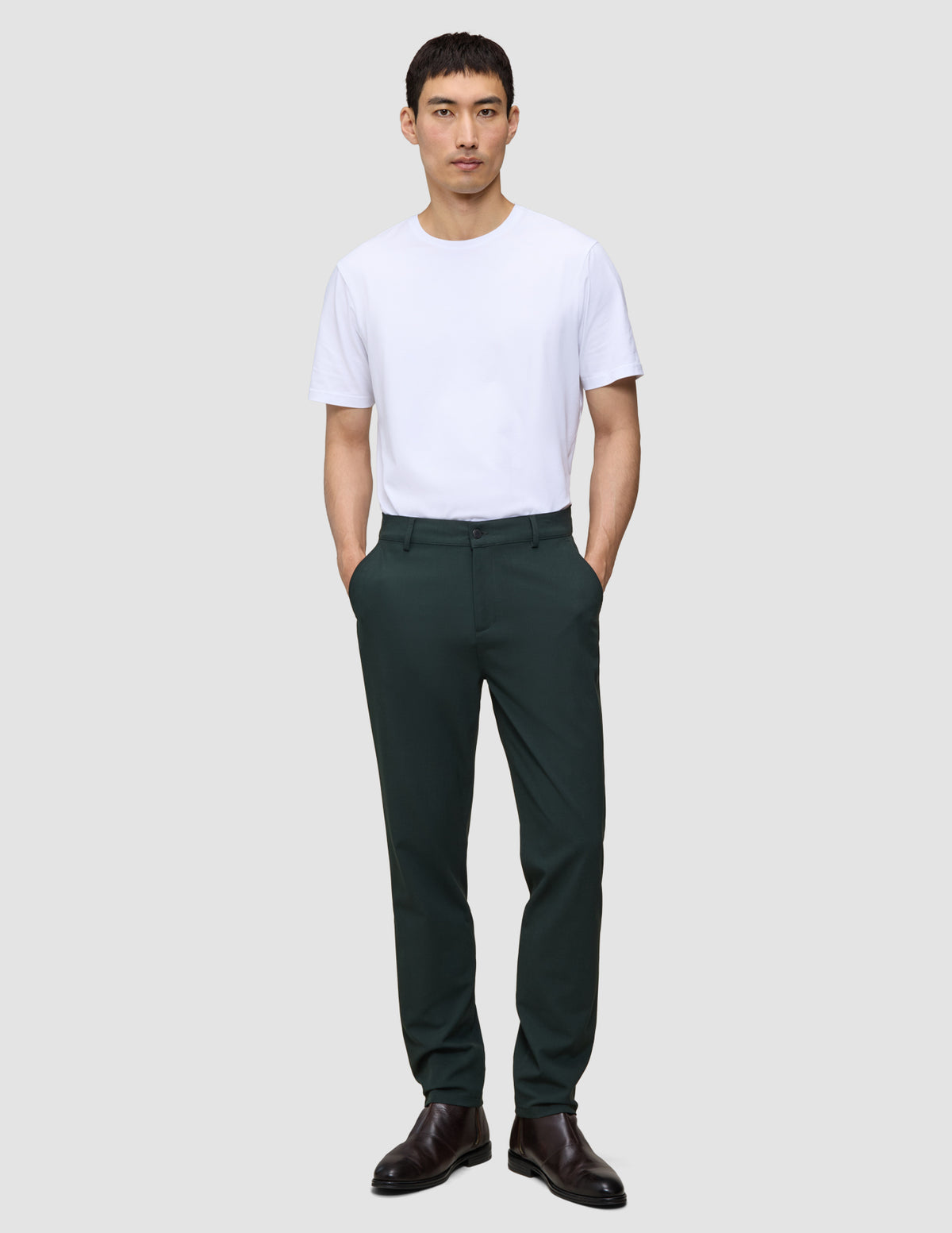 En mand iført en hvid T-shirt og mørkegrønne Ease Pants Regular Northern Pine med hænderne i lommerne.