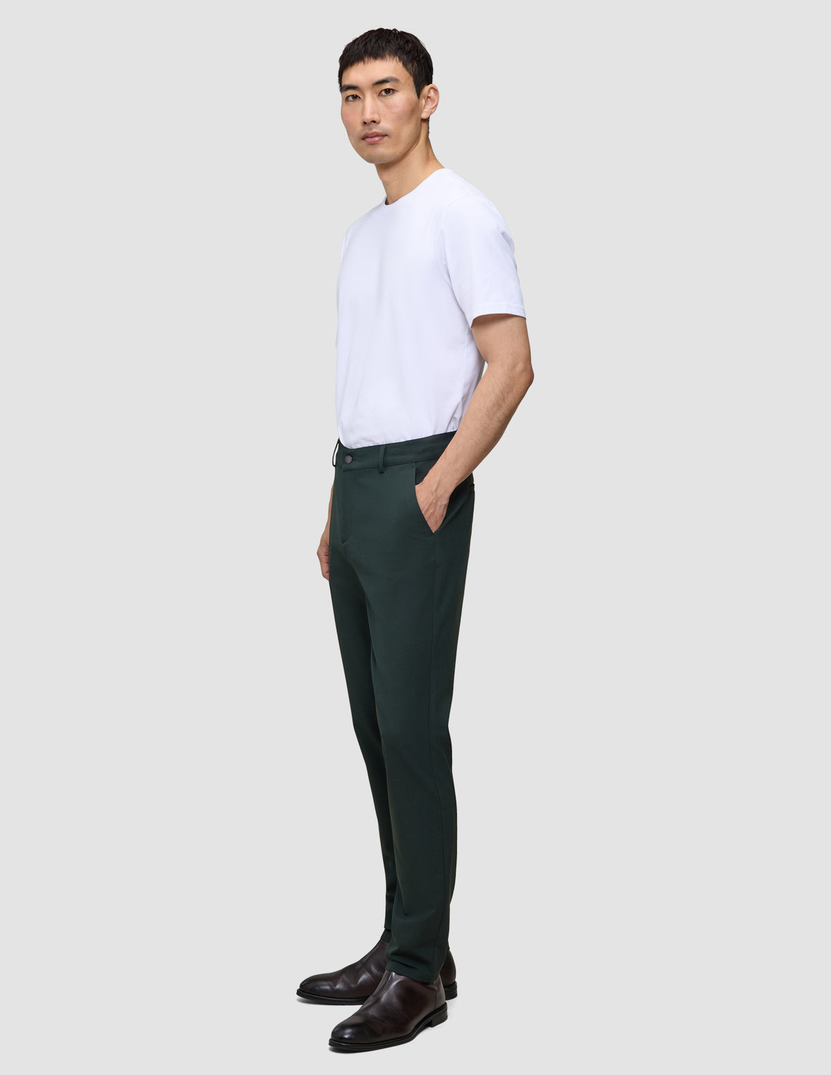 En mand i en hvid T-shirt og Ease Pants Regular Northern Pine står set i profil og fremviser klassisk dansk design.