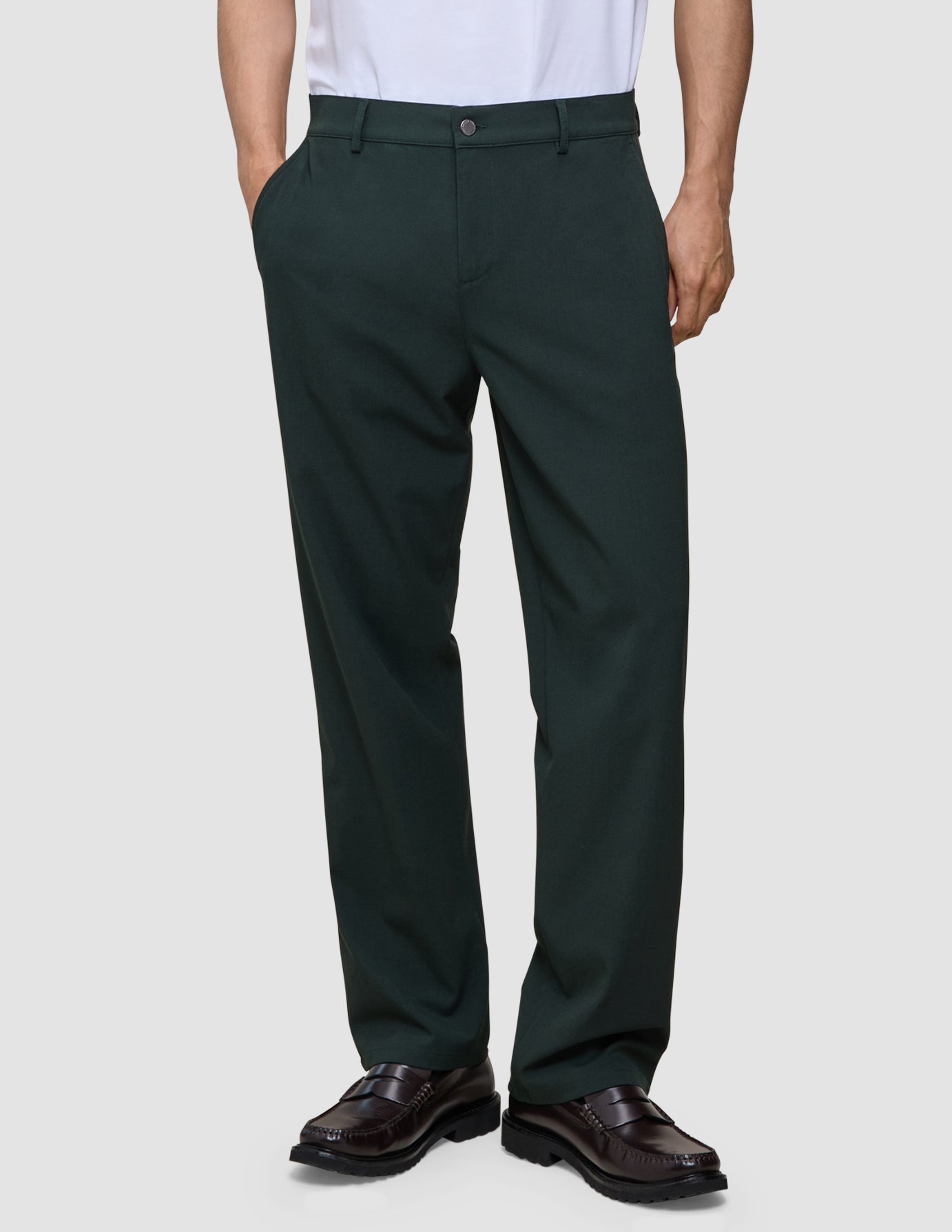 En person iført mørkegrønne Ease Pants i Relaxed Fit-modellen i farven Northern Pine og brune loafers.