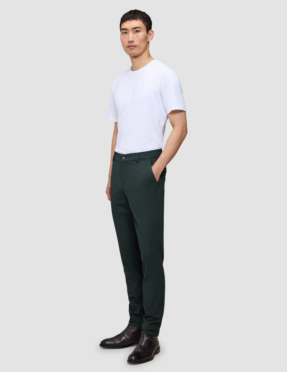 En mand i en hvid T-shirt, Ease Pants Slim Northern Pine med 360°-stretch og mørke læderstøvler.