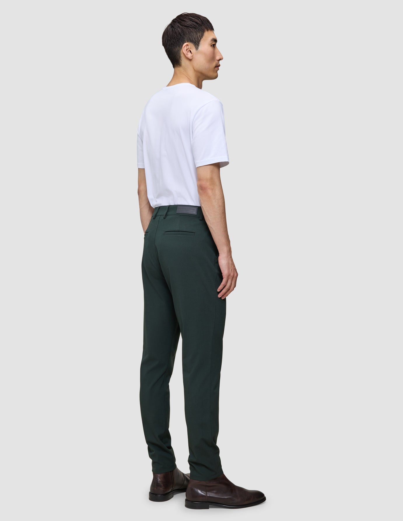 En mand i en hvid T-shirt og Ease Pants Slim Northern Pine står set i profil iført brune læderstøvler.