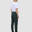 En mand i en hvid T-shirt og Ease Pants Slim Northern Pine står set i profil iført brune læderstøvler.