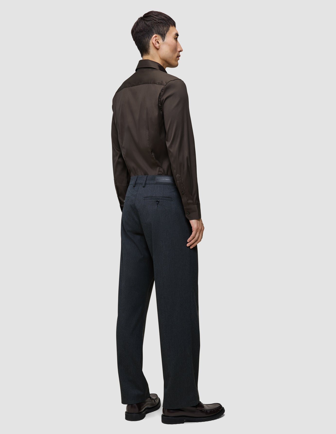 En mand set bagfra iført en Elevated Shirt Regular i mørkebrun, stukket ned i antracitgrå bukser og mørke lædersko.