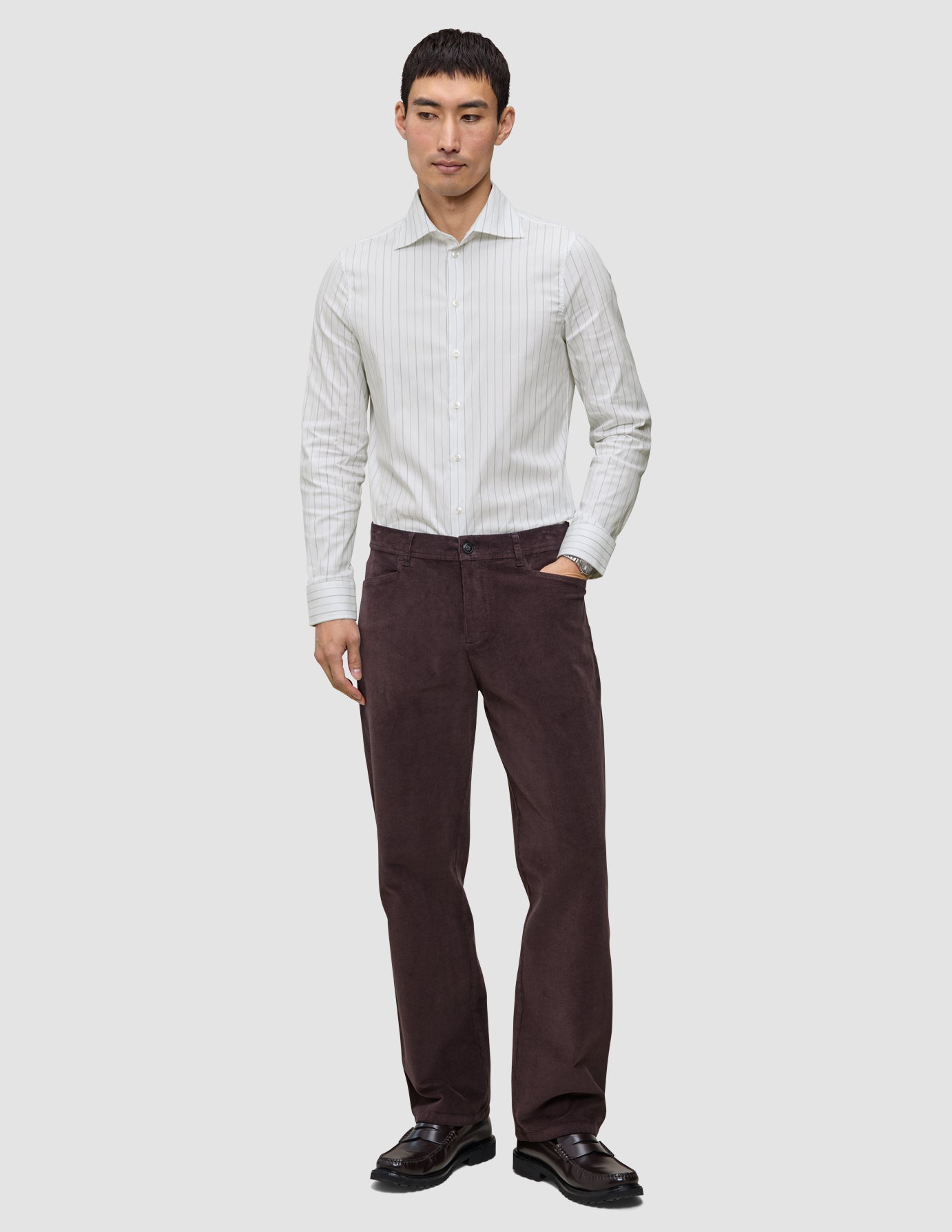 En mand iført en Elevated Shirt Regular i lysegrå striber og mørkebrune bukser.