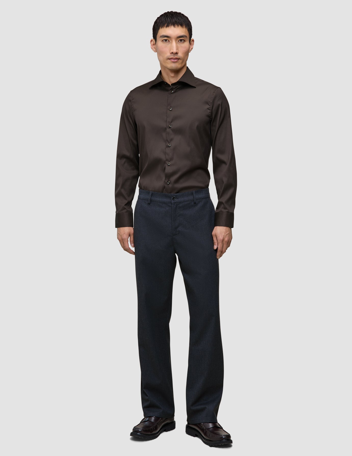 En mand har en mørkebrun Elevated Shirt Slim i Pima-bomuld på sammen med mørke bukser og fine sko.