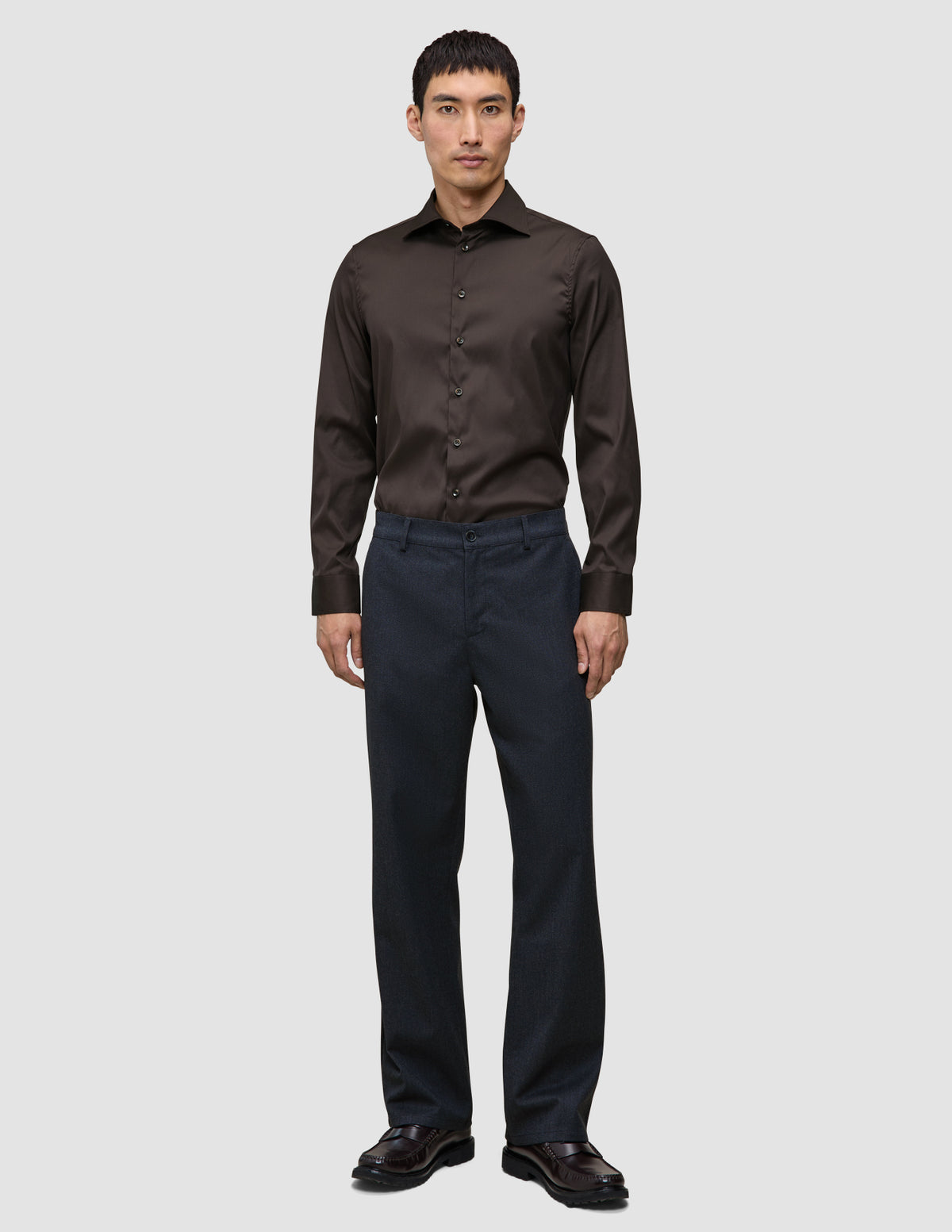 En mand har en mørkebrun Elevated Shirt Slim i Pima-bomuld på sammen med mørke bukser og fine sko.