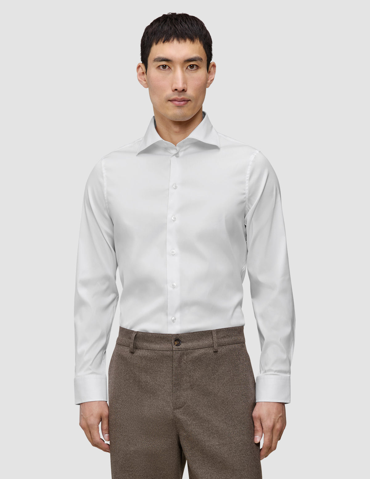 En mand iført en hvid, slim-fit langærmet skjorte med knapper, der er stoppet ned i brune bukser.