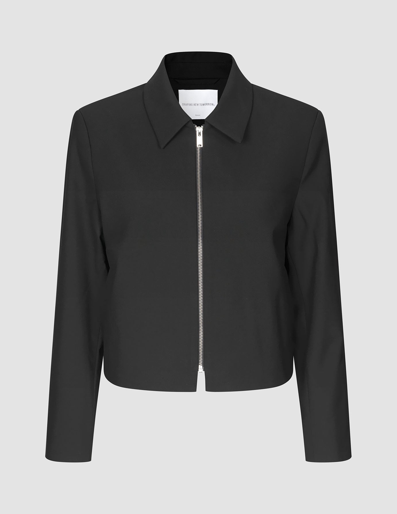 Essential Short Zip Jacket Black, en minimalistisk sort jakke med en sølvfarvet lynlås i fuld længde foran.