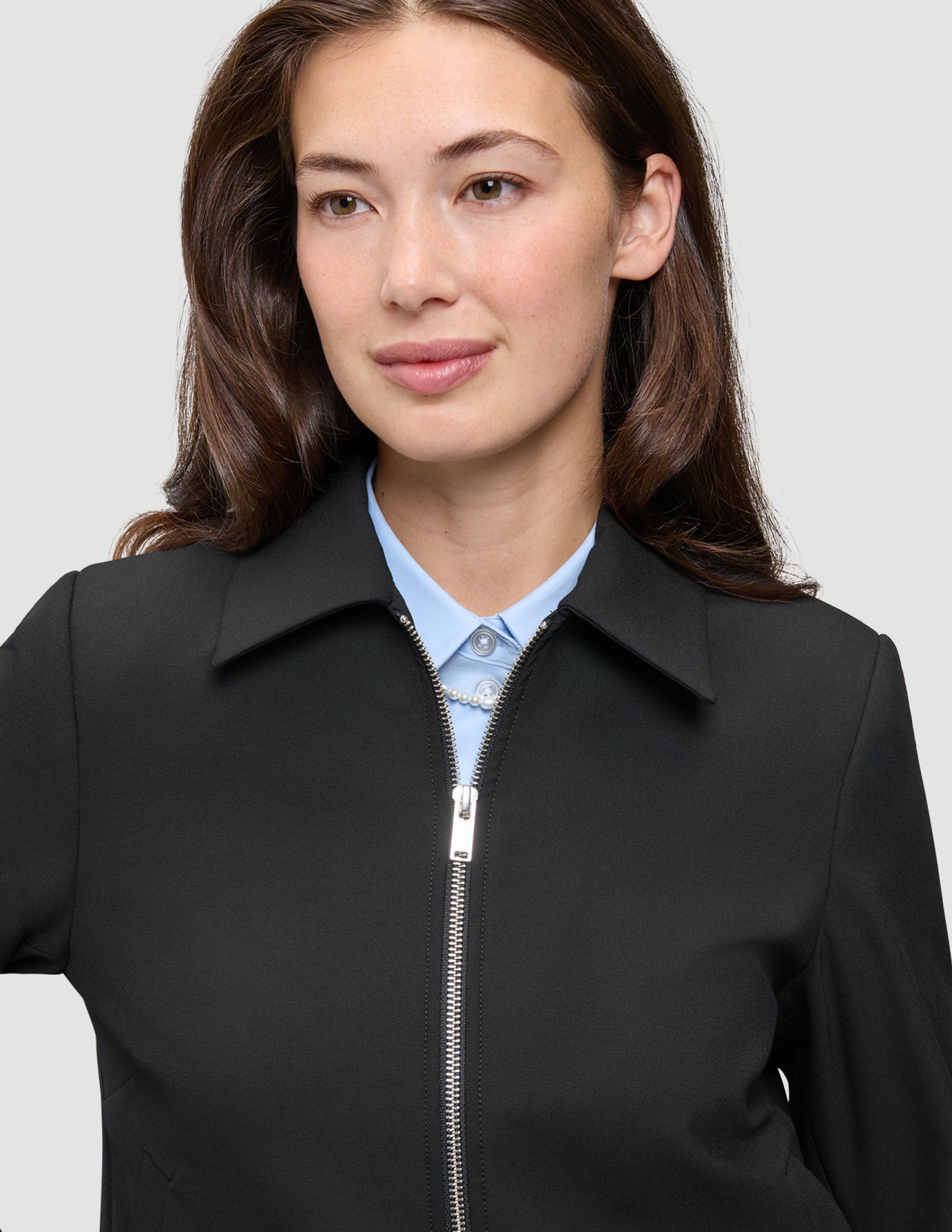 En person, der har en sort Essential Short Zip Jacket på over en lyseblå skjorte med krave.
