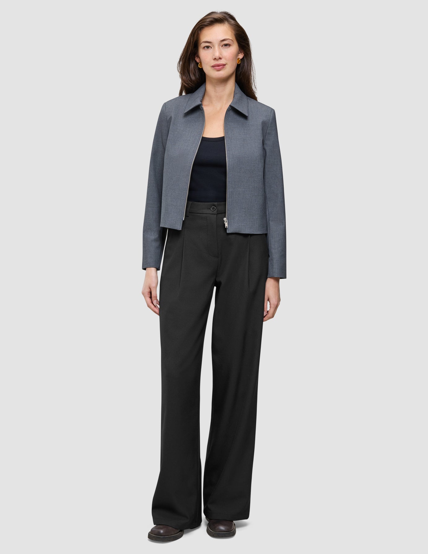 En kvinde har en Essential Short Zip Jacket i mørkegrå melange på over en sort top og sorte bukser.
