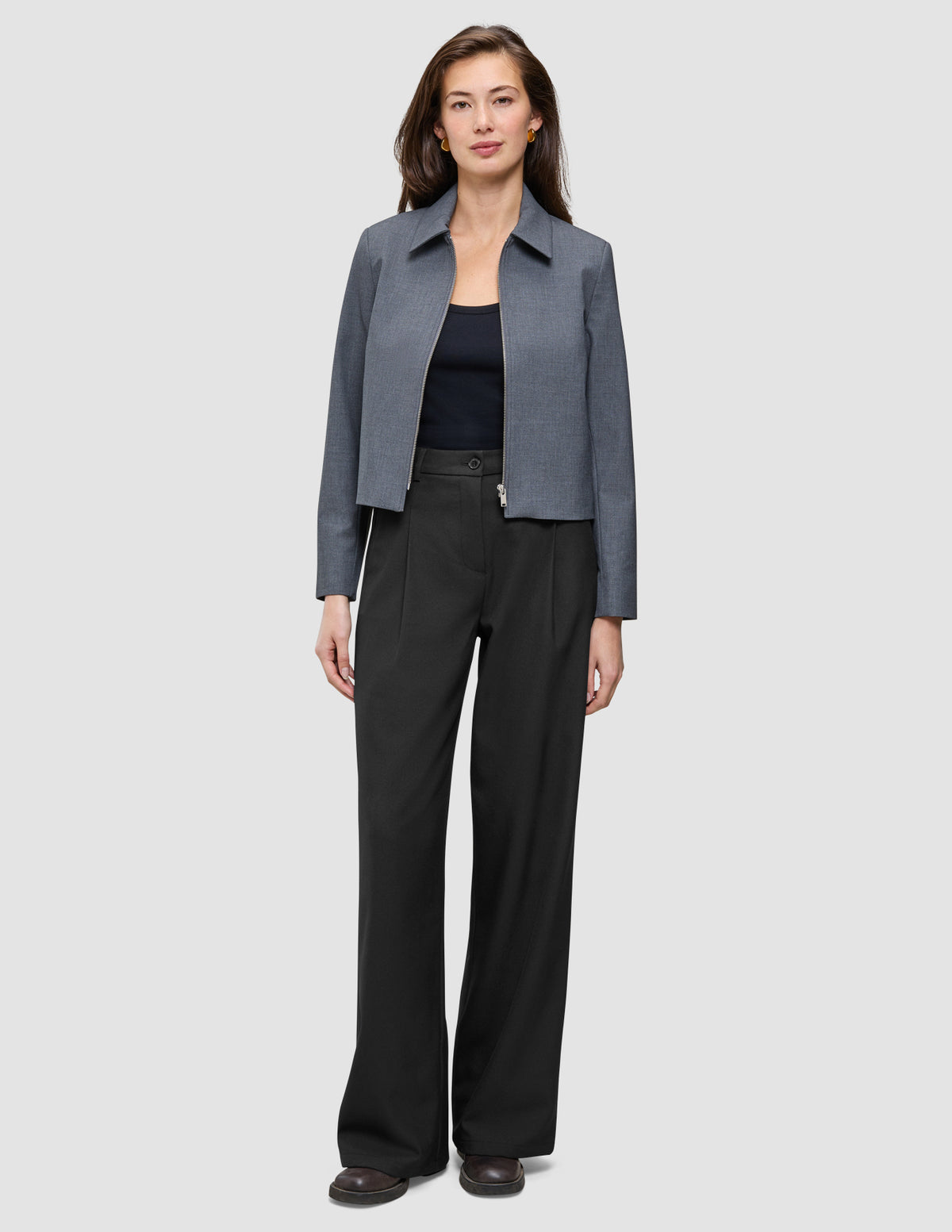 En kvinde har en Essential Short Zip Jacket i mørkegrå melange på over en sort top og sorte bukser.
