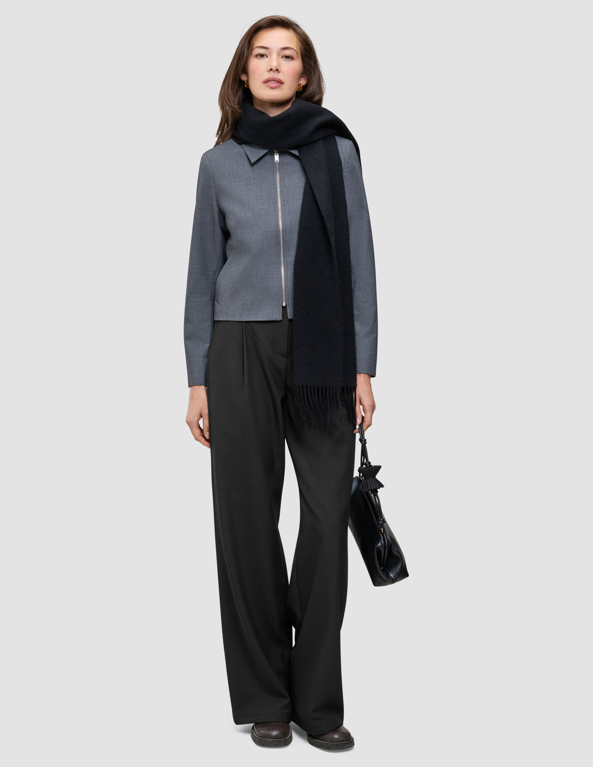 En kvinde har en Essential Short Zip Jacket i mørkegrå melange på sammen med sorte bukser, et tørklæde og en sort håndtaske.