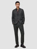 En mand har en Motion Blazer Regular i farven Pepper Grey på over en mørk skjorte med knapper og loafers.