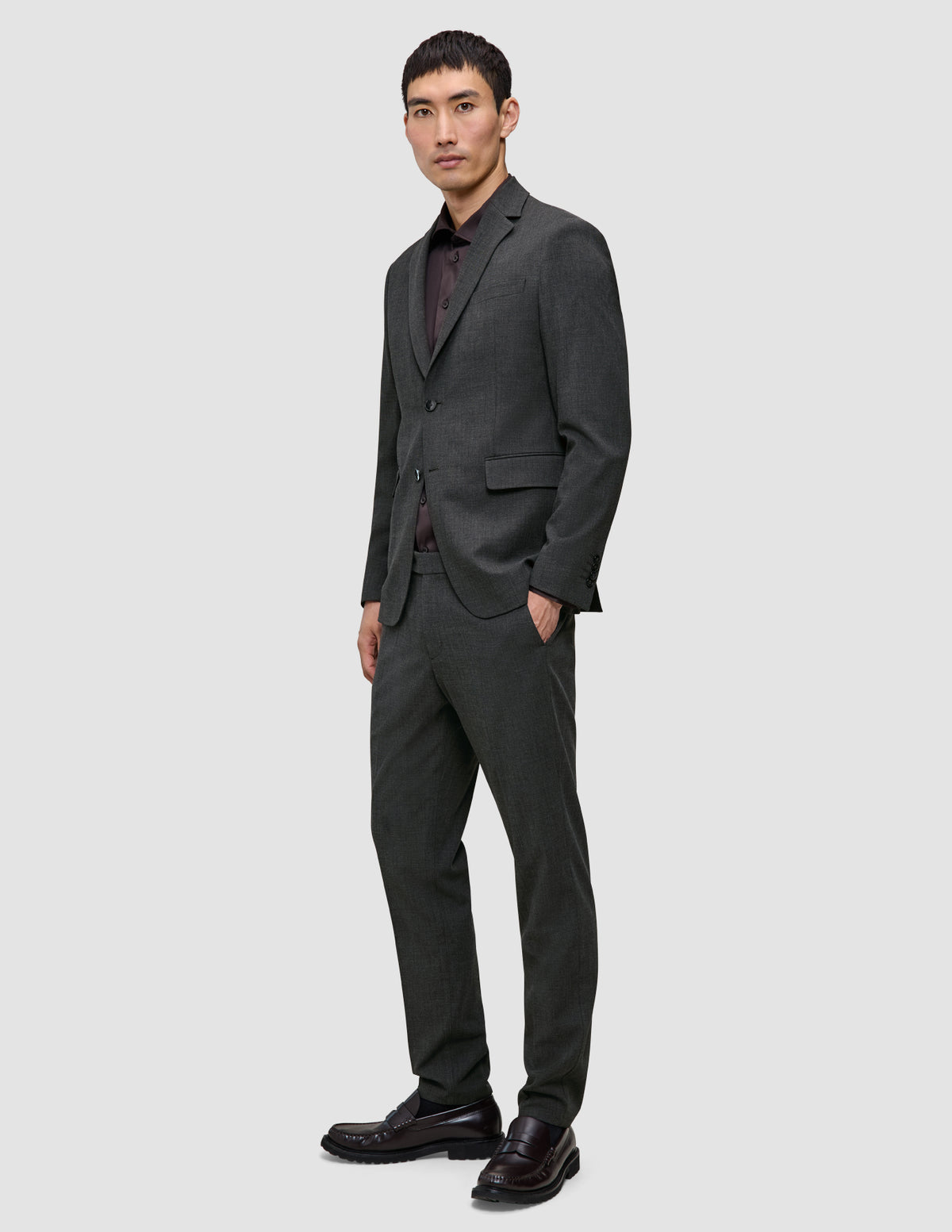 En mand iført en Motion Blazer Regular i farven Pepper Grey, en mørk skjorte med knapper, matchende bukser og loafers i dansk design.