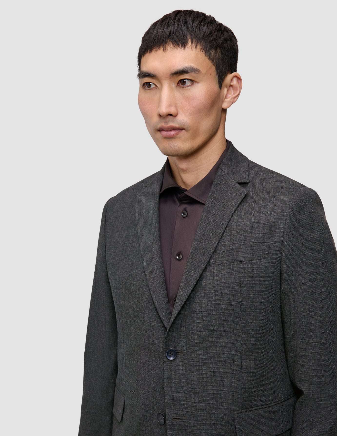 En mand iført en grå Motion Blazer Regular Pepper Grey over en mørk skjorte med knapper, der fremhæver det rene danske design.