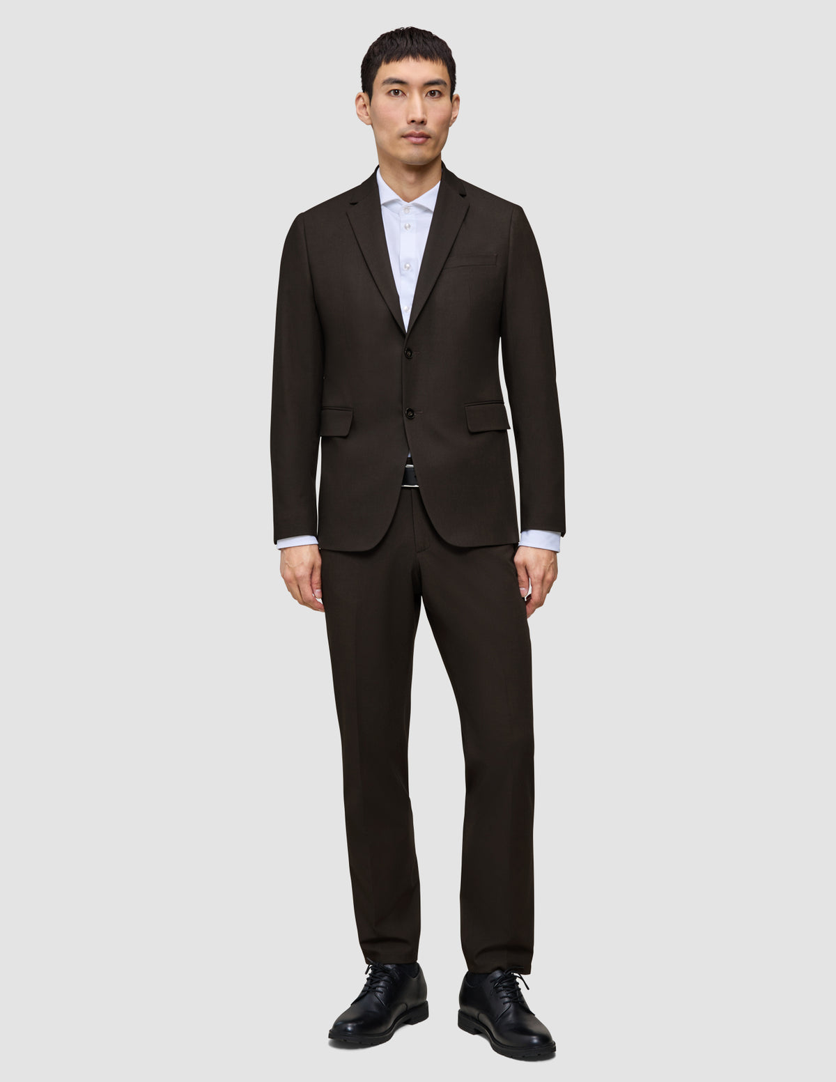 En mand iført en mørkebrun Motion Blazer Slim Cognac, en hvid skjorte og sorte herresko.