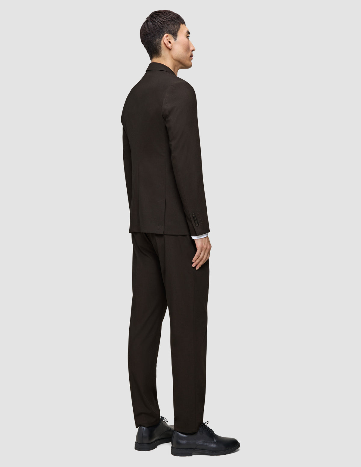 Set fra siden: En person iført en mørkebrun Motion Blazer Slim Cognac og sorte sko, der er indbegrebet af moderne dansk design.