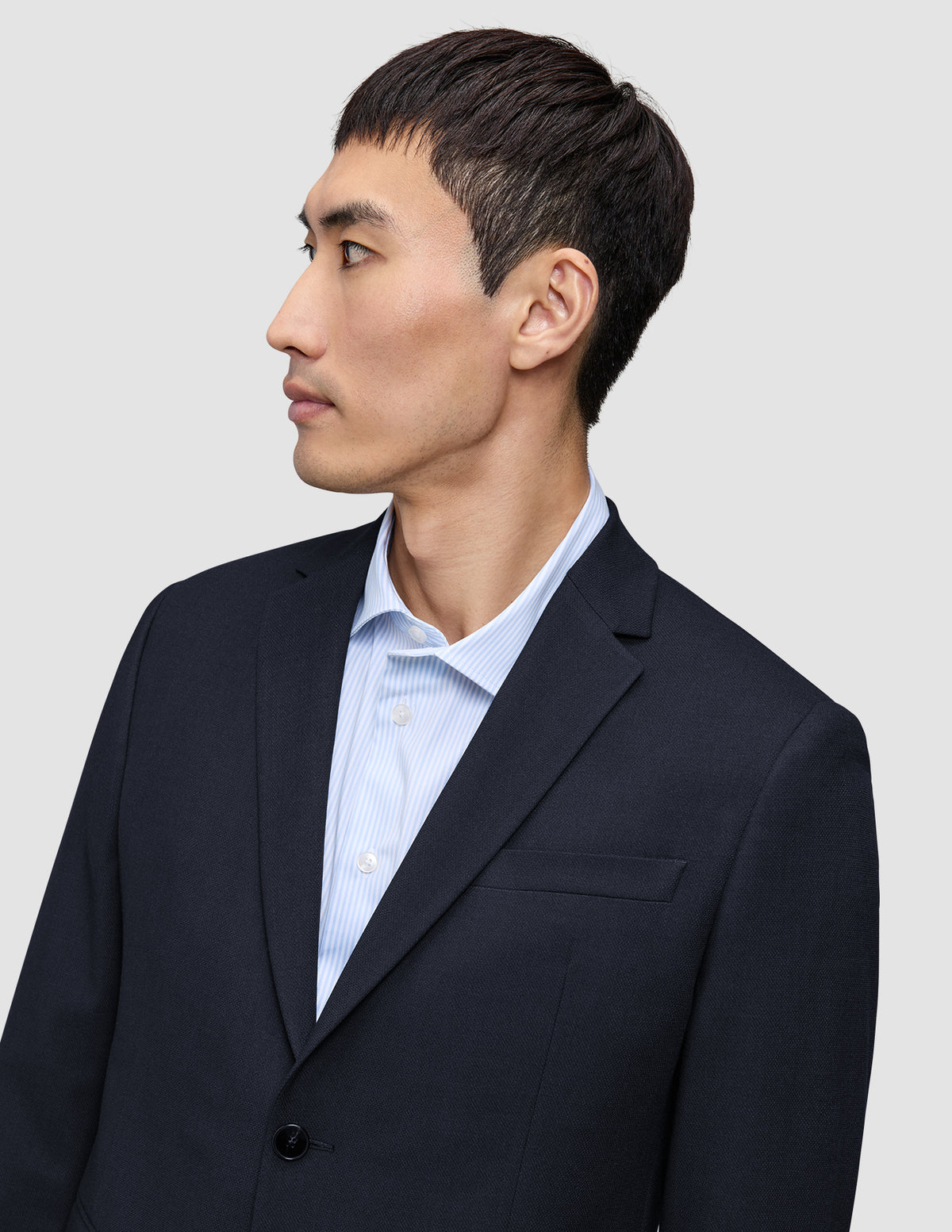En person set i profil har en mørkeblå Motion Blazer Slim Midnight Blue på over en lyseblå stribet skjorte.