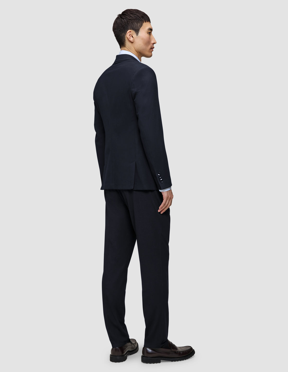 En mand set bagfra, iført en Motion Blazer Slim Midnight Blue-jakke og -bukser samt loafers.