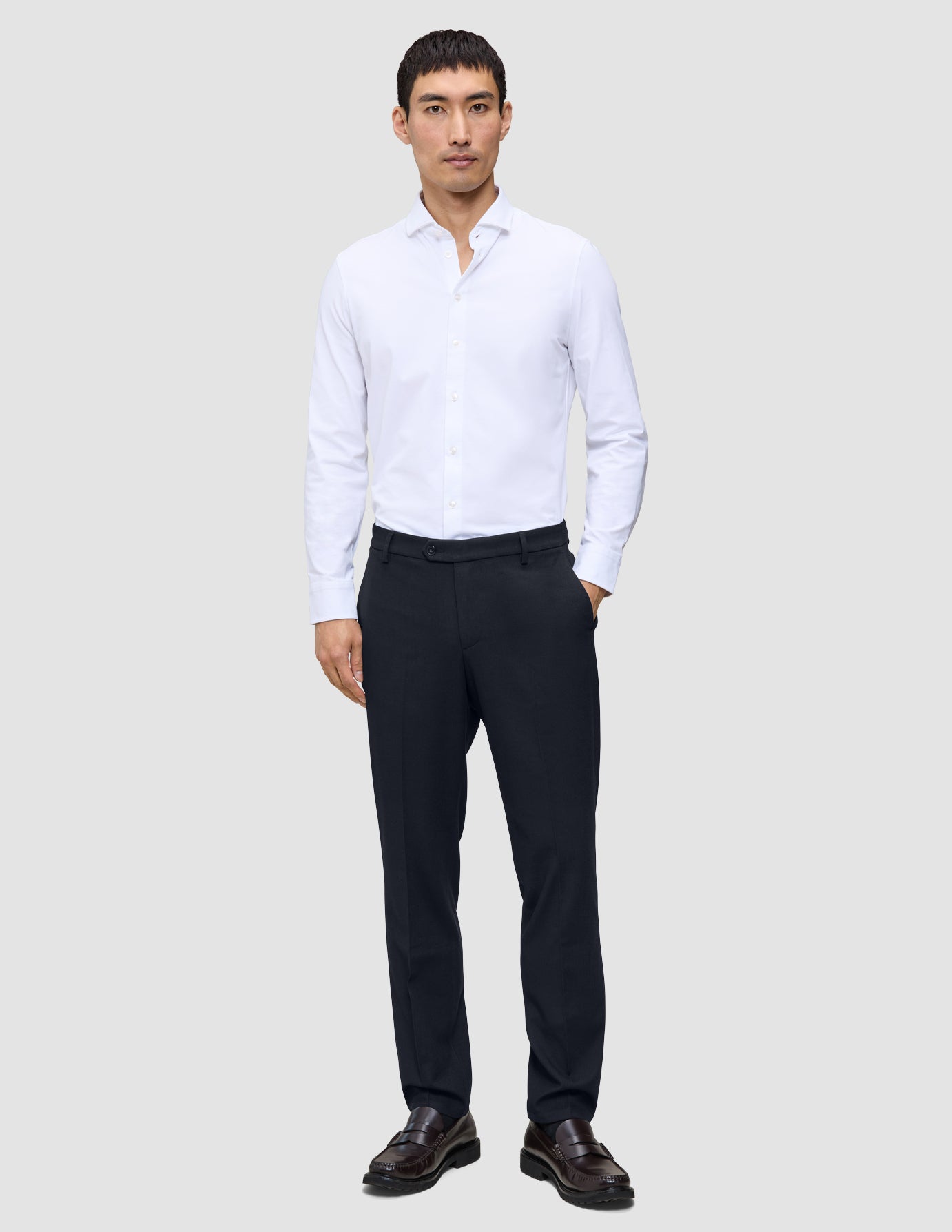 En mand iført en hvid skjorte med knapper, Motion Suit-bukser i regular-pasform i midnatsblå og læderloafers.