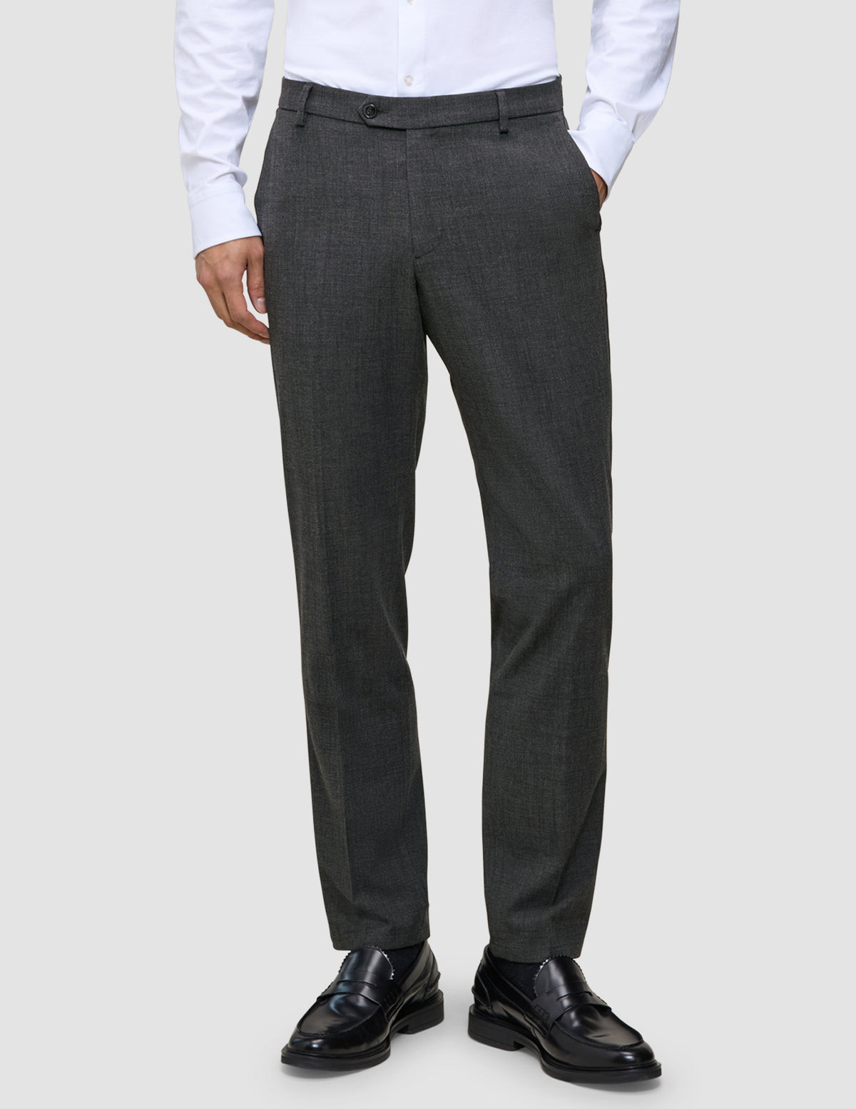 En person har grå Motion Suit-bukser i farven Regular Pepper Grey på, en hvid skjorte med knapper og sorte læderloafers.