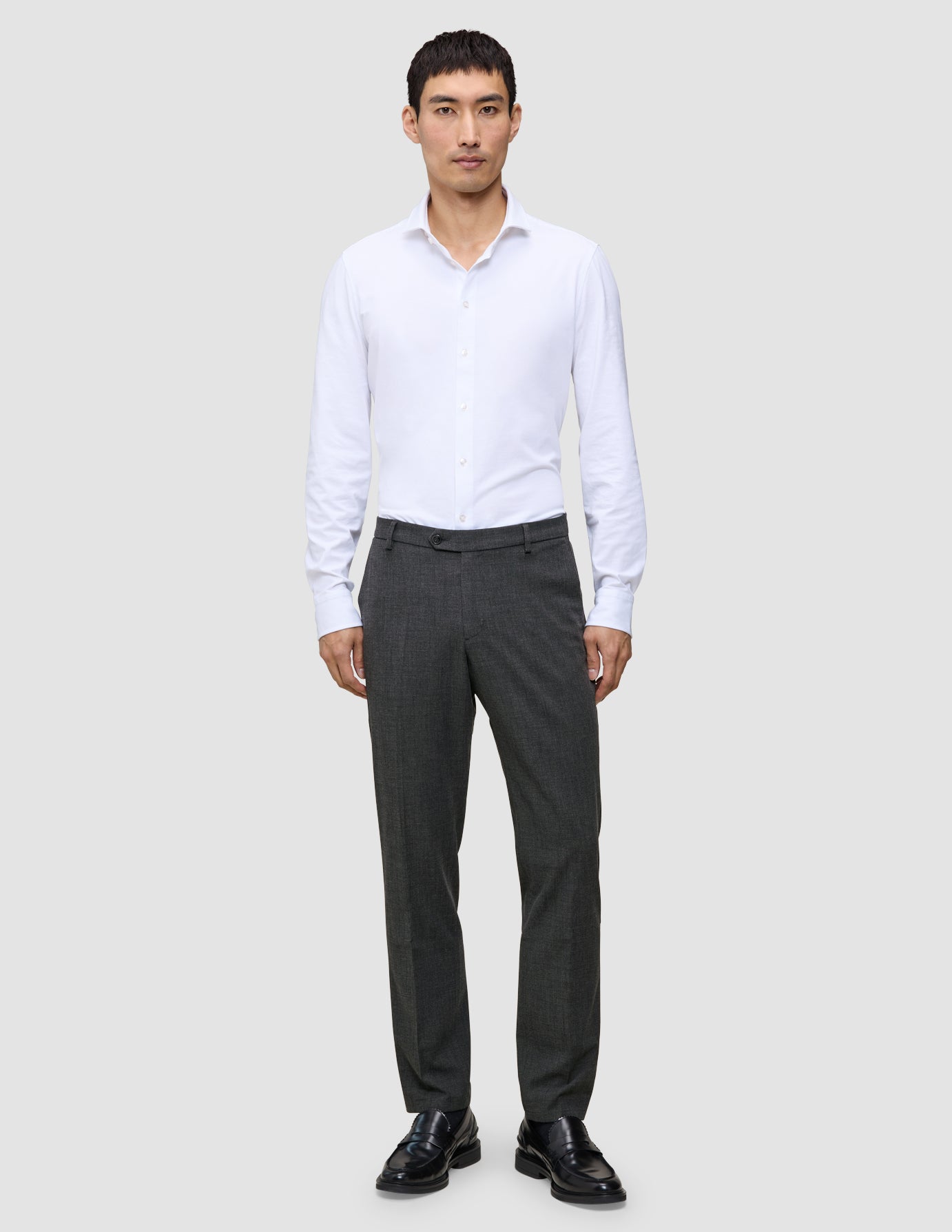 En mand i en hvid skjorte med knapper og et par Motion Suit-bukser i farven Regular Pepper Grey.