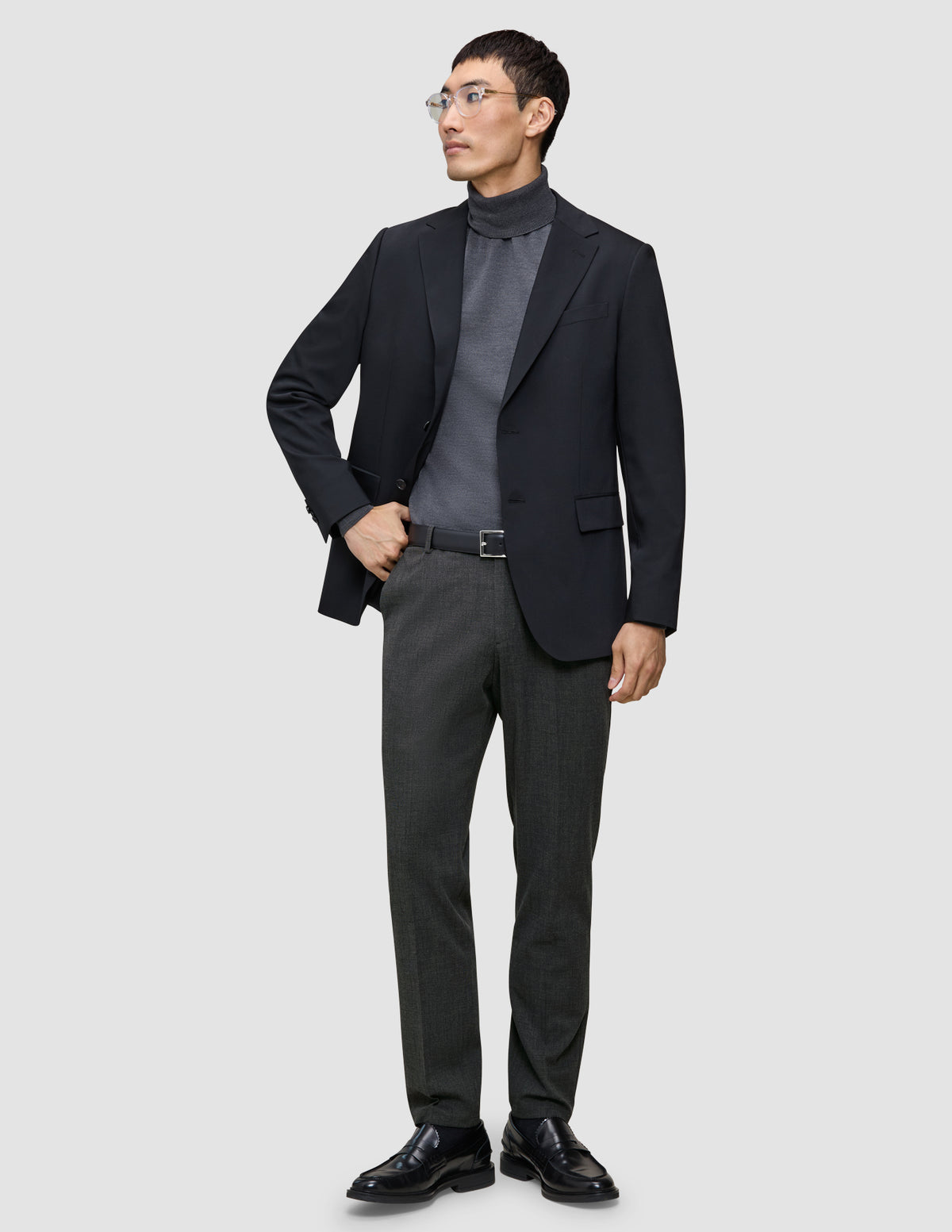 En mand i en sort blazer, en grå rullekravebluse og et par Motion Suit-bukser i farven Regular Pepper Grey.