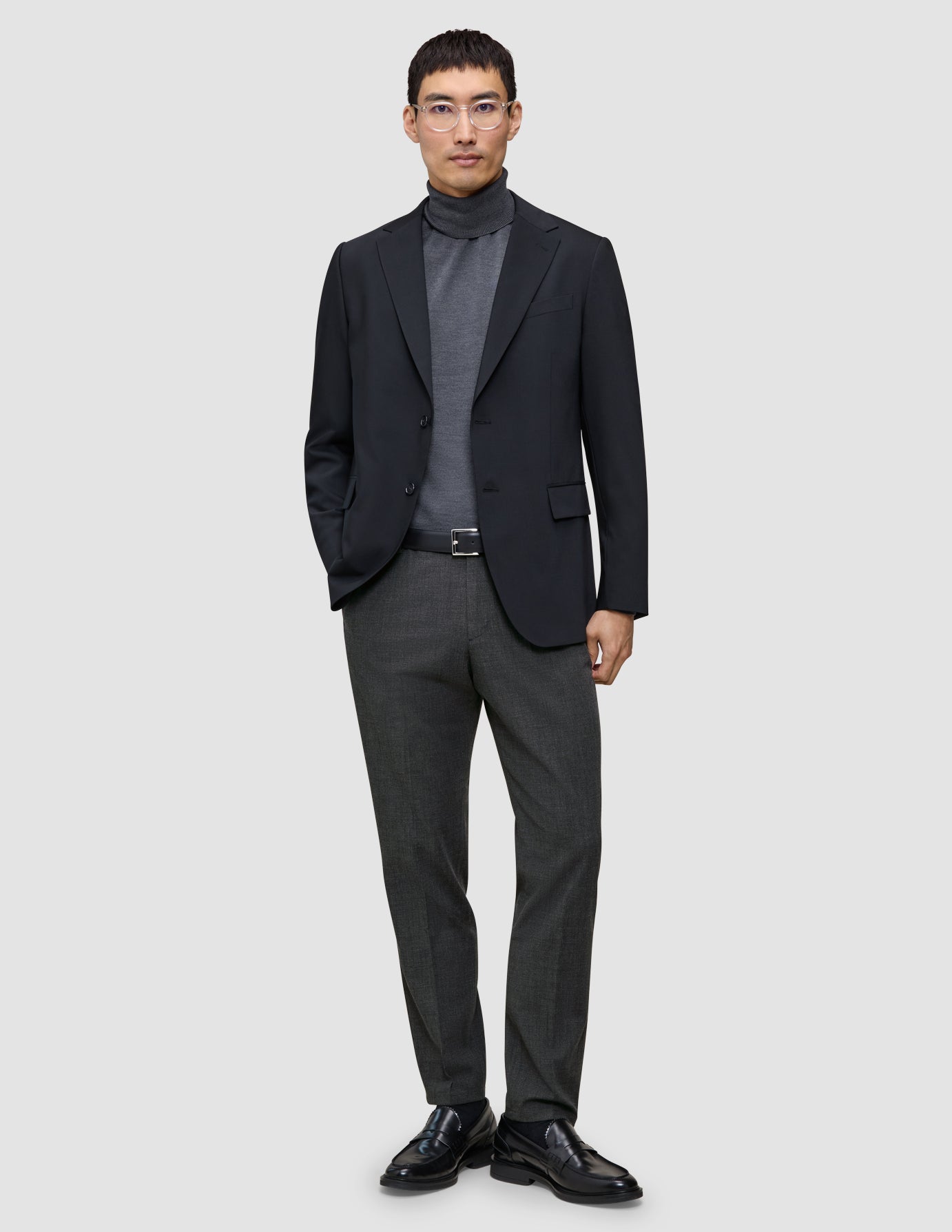 En mand iført en sort blazer, en grå rullekravebluse, Motion Suit-bukser i Regular-pasform i farven Pepper Grey og sorte loafers.