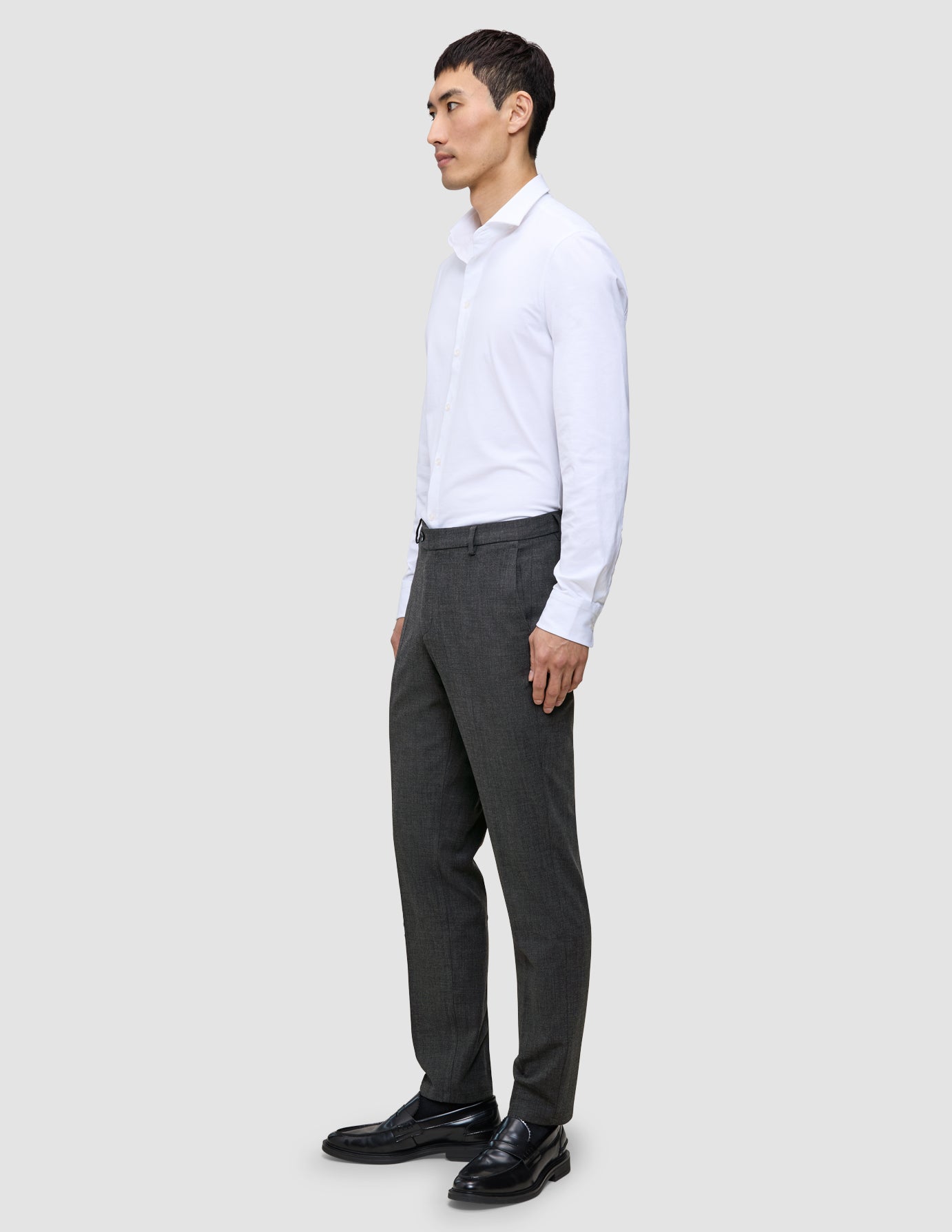 En mand i en hvid skjorte og Motion Suit-bukser i Regular Pepper Grey står set i profil og er indbegrebet af det rene danske design.