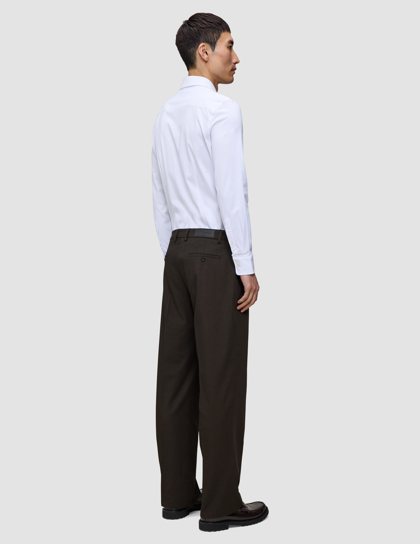 Set fra siden: en mand i en hvid skjorte med knapper og Motion Suit-bukser i modellen Relaxed i farven Cognac.