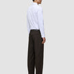 Set fra siden: en mand i en hvid skjorte med knapper og Motion Suit-bukser i modellen Relaxed i farven Cognac.