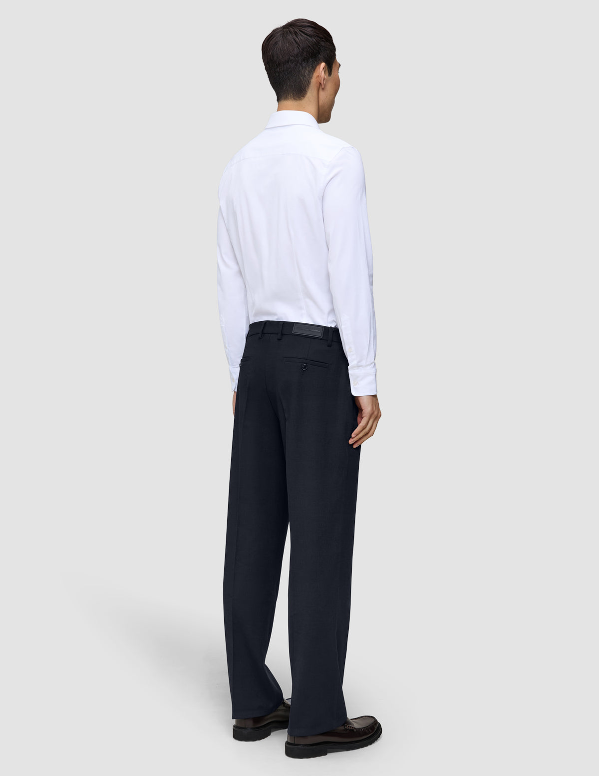 En mand set bagfra, iført en hvid skjorte med knapper og et par Motion Suit-bukser i afslappet pasform i midnatsblå.