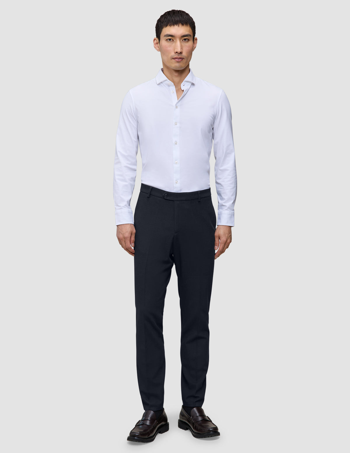 En mand iført en hvid skjorte med knapper, Motion Suit-bukser i slim fit i midnatsblå og mørkebrune loafers.
