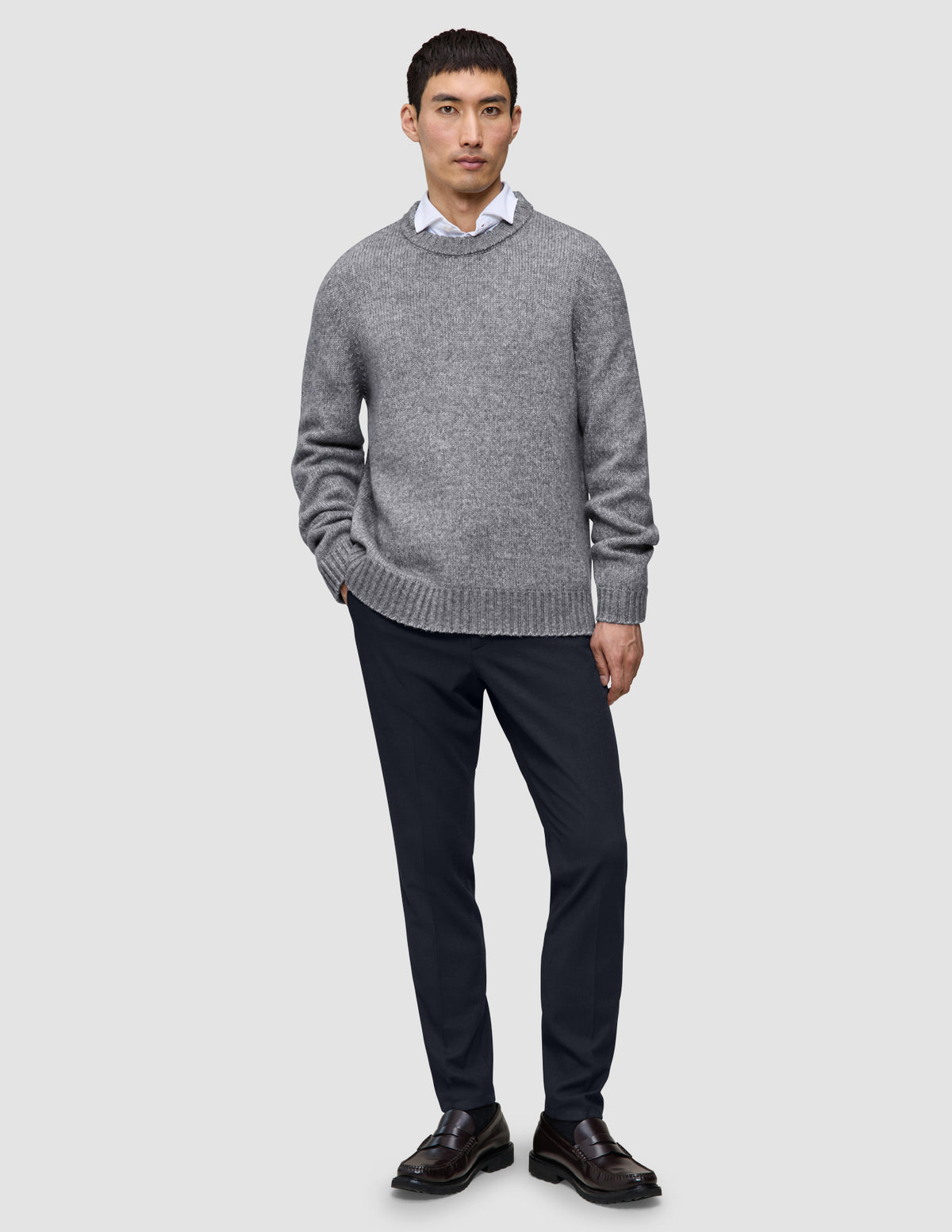 En mand har en grå trøje, en hvid skjorte, Motion Suit-bukser i slim fit i midnatsblå og mørke læderloafers på.