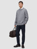 En mand iført en grå sweater, en hvid skjorte og et par Midnight Blue Motion-bukser i slim-fit, der holder en brun rejsetaske.