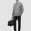 En mand iført en grå sweater, en hvid skjorte og et par Midnight Blue Motion-bukser i slim-fit, der holder en brun rejsetaske.