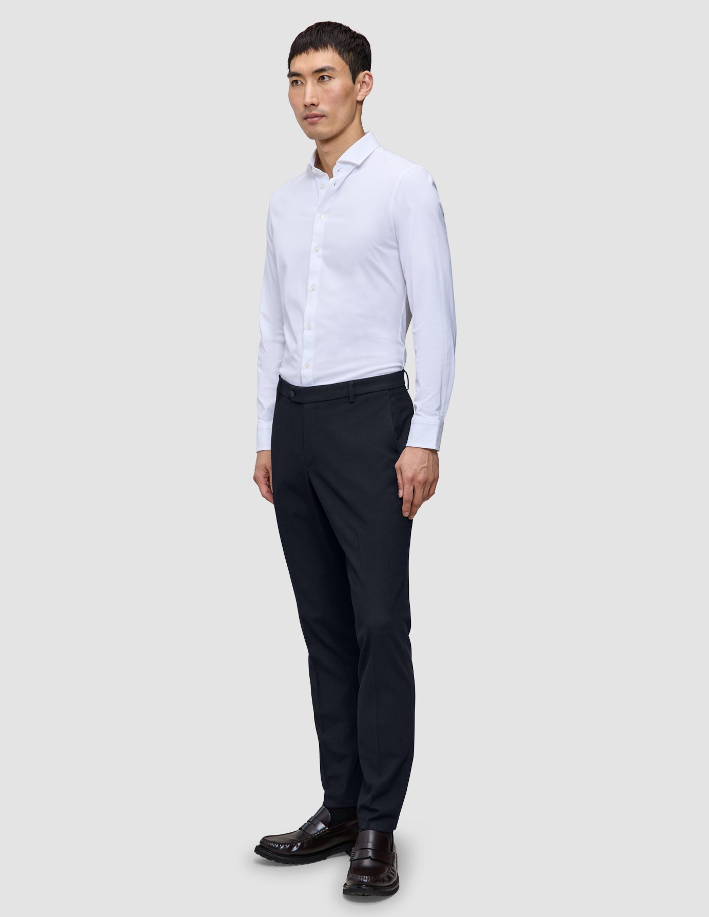 En mand i en hvid skjorte med knapper og et par Motion Suit-bukser i slim fit i midnatsblå, der fremhæver klassisk dansk design.