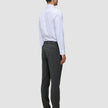 En mand i en hvid skjorte med knapper og grå Motion Suit-bukser i farven Slim Pepper Grey står med ryggen til kameraet.
