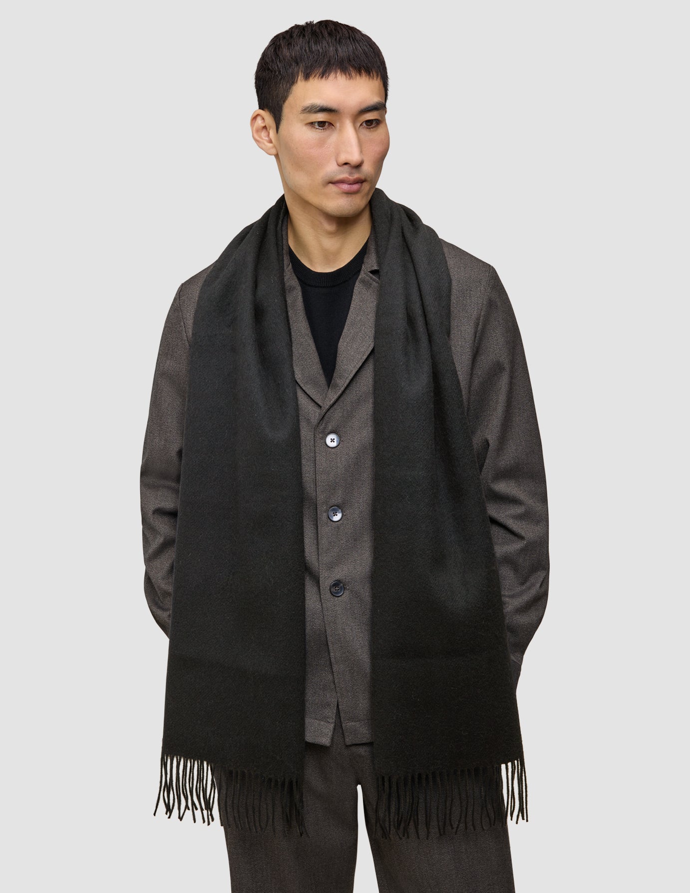 En mand, der bærer et sort tørklæde med frynser i kanten over en grå blazer.