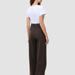 En person set bagfra, iført en hvid T-shirt og mørkebrune Serene Pants Wide Walnut Herringbone-bukser med høj talje og brede ben.